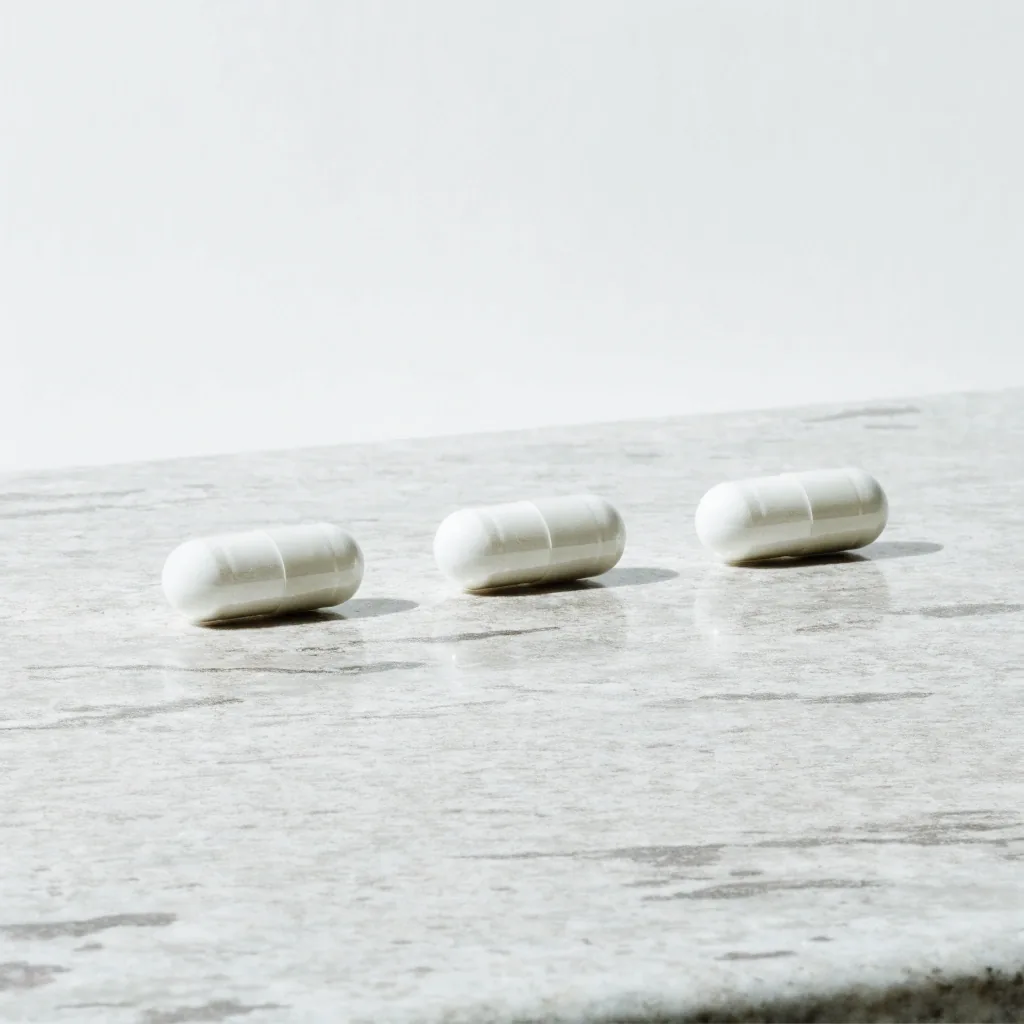 Three hard capsules with visible seams arranged in a row on granite-look stone