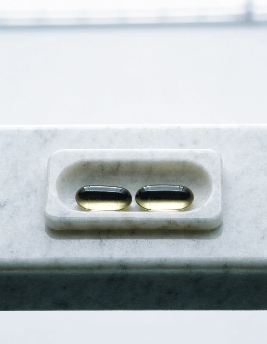 Two translucent softgel capsules in a recessed well of a granite-look tray