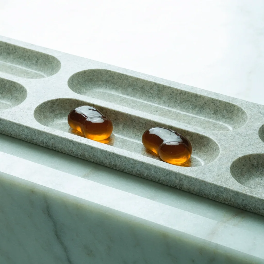 Two cast gel gummy multivitamin shapes resting in the well of a granite sorting tray under even skylight
